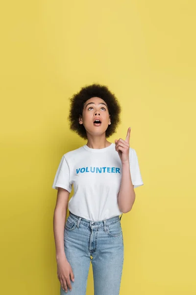 Surprised african american volunteer looking up and pointing with finger isolated on yellow — Stockfoto