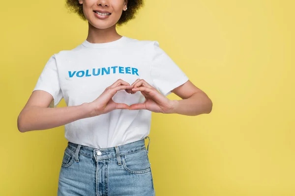 Partial view of happy african american volunteer showing heart symbol with hands isolated on yellow — Stock Photo