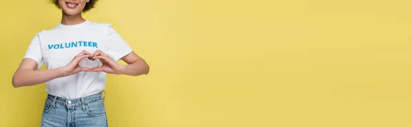 Partial view of african american volunteer showing love sign with hands isolated on yellow, banner - foto de stock