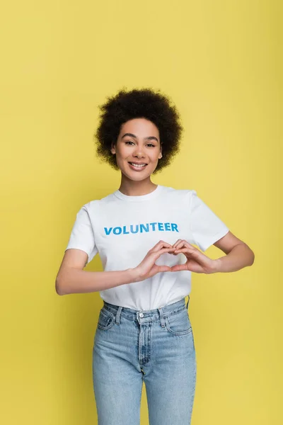 Young african american volunteer showing heart symbol with hands isolated on yellow — Stock Photo