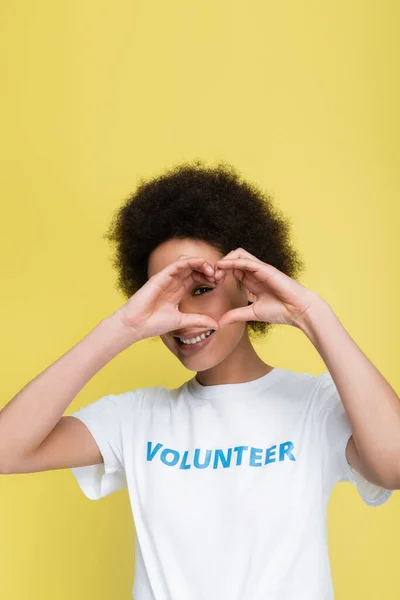 Cheerful african american volunteer showing heart sign near face isolated on yellow — Stock Photo