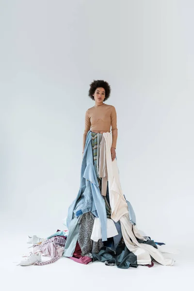 Brunette african american woman standing on pile of garments on grey background — Stock Photo