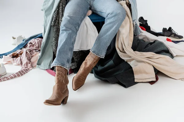 Partial view of woman in jeans and cowboy boots near pile of clothes on grey background — Stock Photo