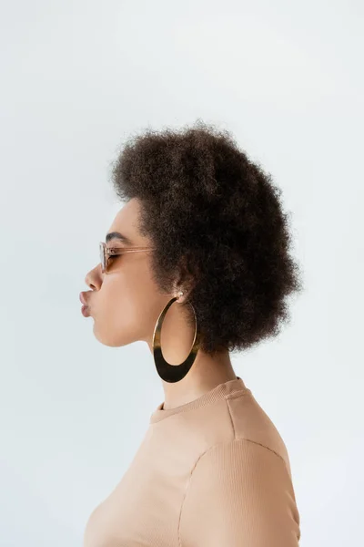 Vista laterale della donna afroamericana in occhiali da sole e anello orecchino labbra bronzanti isolato su grigio — Foto stock