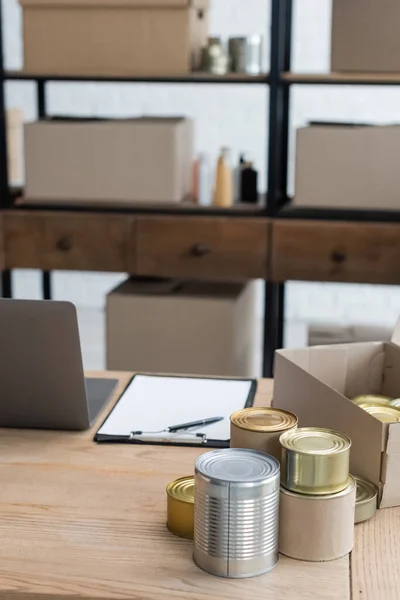 Nourriture en conserve et presse-papiers près de l'ordinateur portable sur le bureau dans le centre de bienfaisance — Photo de stock