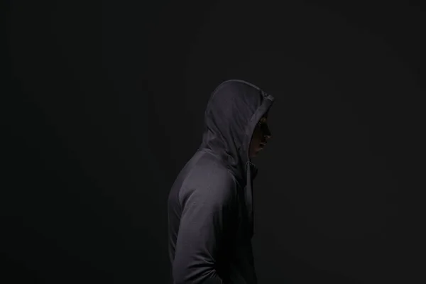Вид сбоку на африканского американского хулигана в капюшоне, стоящего изолированно на черном — стоковое фото