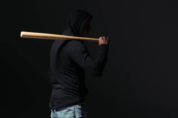 Side view of african american hooligan holding baseball bat isolated on black - foto de stock