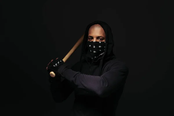 Gamberro afroamericano con máscara en la cara sosteniendo bate de béisbol aislado en negro - foto de stock