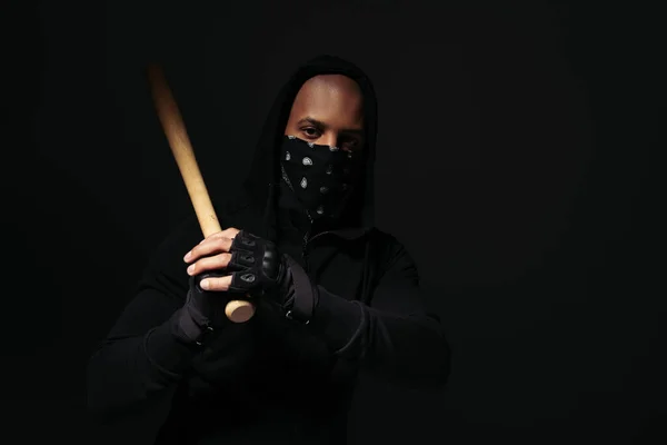 African american hooligan in mask on face and glove holding baseball bat isolated on black — Stockfoto