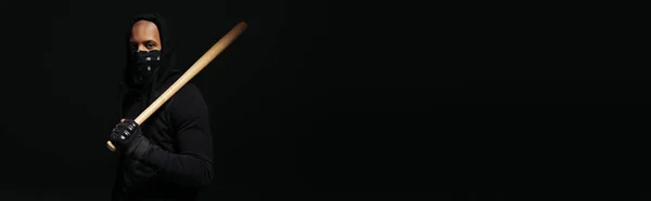 African american hooligan with mask on face holding baseball bat isolated on black, banner - foto de stock