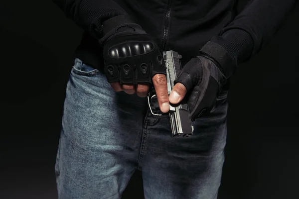 Vista recortada de bandido afroamericano en guantes con pistola aislada en negro - foto de stock