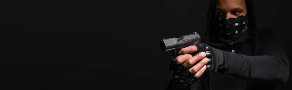 Blurred african american bandit holding handgun isolated on black, banner — Stock Photo