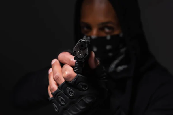 Blurred african american bandit in gloves holding handgun isolated on black - foto de stock