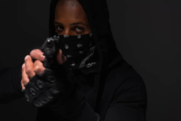 African american bandit with mask on face holding blurred gun isolated on black — Photo de stock