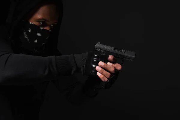 Bandit afro-américain au visage obscur tenant une arme isolée sur du noir — Photo de stock