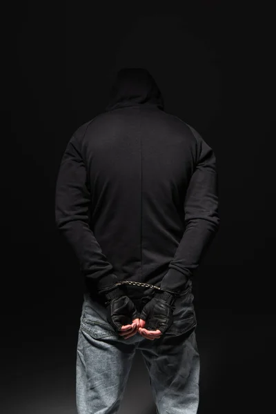 Back view of african american bandit in hoodie and handcuffs standing isolated on black — Stockfoto