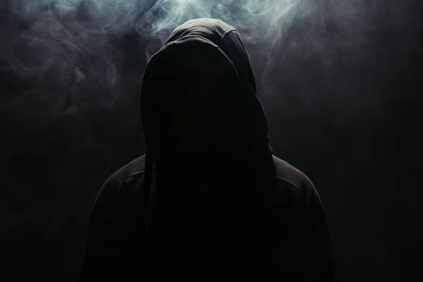 Silhouette of hooligan in hood on black background with smoke — Stock Photo