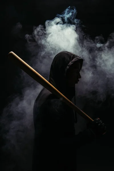 Side view of silhouette of hooligan with baseball bat on black background with smoke — Photo de stock