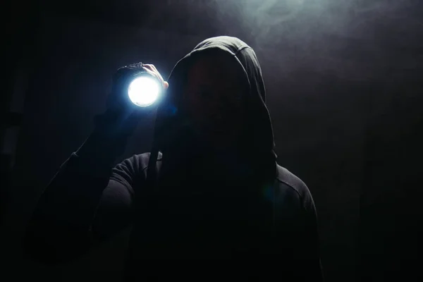 Silhouette of hooligan holding flashlight on black background with smoke — Stock Photo