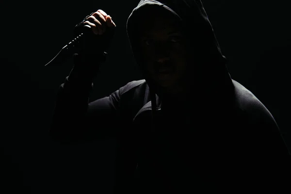 Silhouette of hooligan in hoodie holding knife isolated on black with lighting — Stockfoto