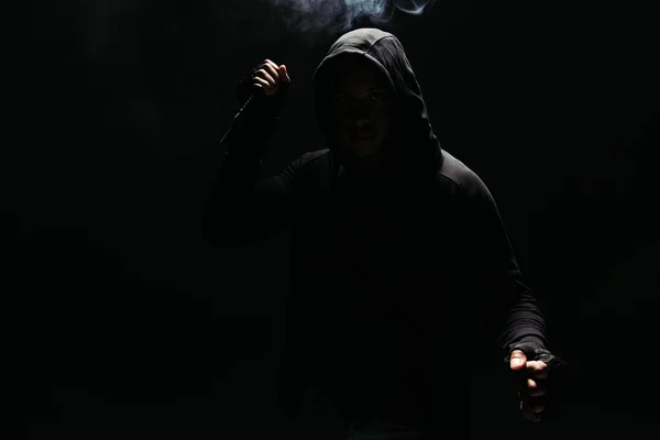 Silhouette of african american bandit in hoodie in gloves holding knife on black background with smoke — Photo de stock