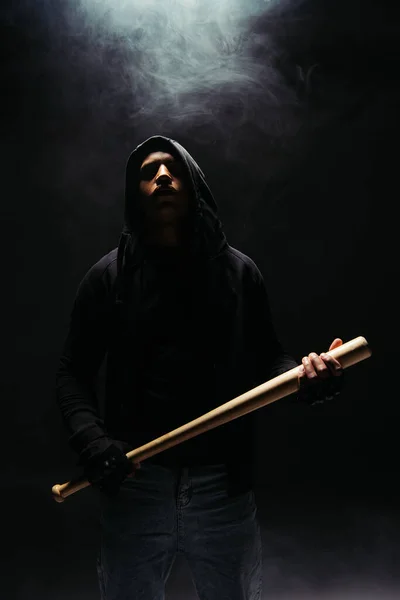 African american hooligan in hoodie holding baseball bat on black background with lighting and smoke — Fotografia de Stock