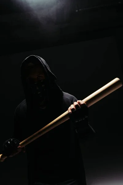 Silhouette of african american vandal holding wooden baseball bat on black background with smoke — Stockfoto