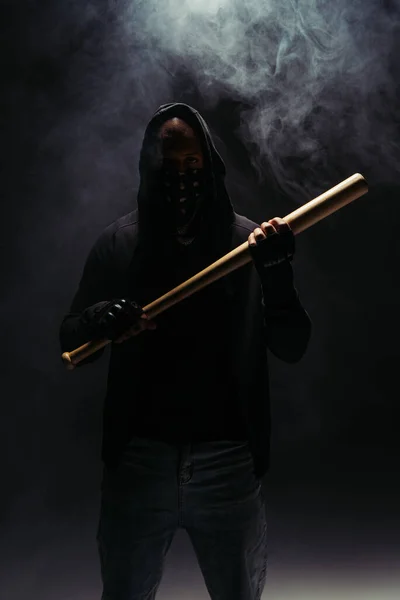 Silhouette of african american bandit with mask on face holding baseball bat on black background with smoke — Fotografia de Stock