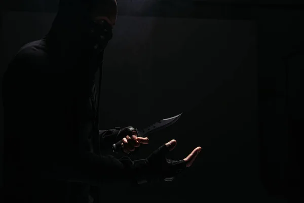 Side view of african american bandit in mask holding knife isolated on black — Stock Photo