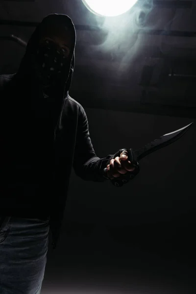Silhouette of african american hooligan with obscure face holding knife on black background with smoke — Fotografia de Stock