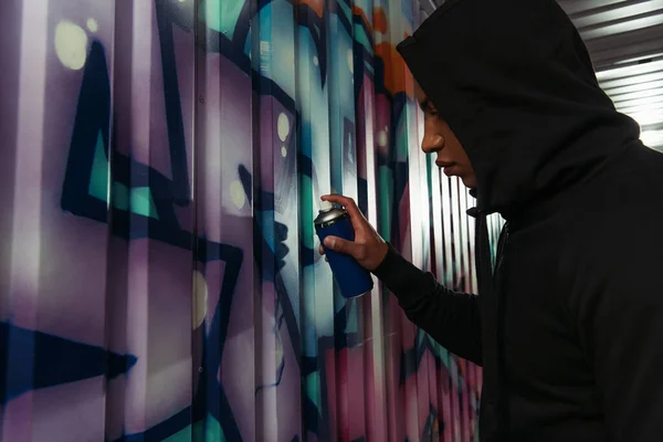 Side view of african american vandal in hood drawing graffiti on wall — Photo de stock