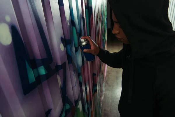 Side view of african american vandal with spray paint drawing graffiti on wall — Photo de stock