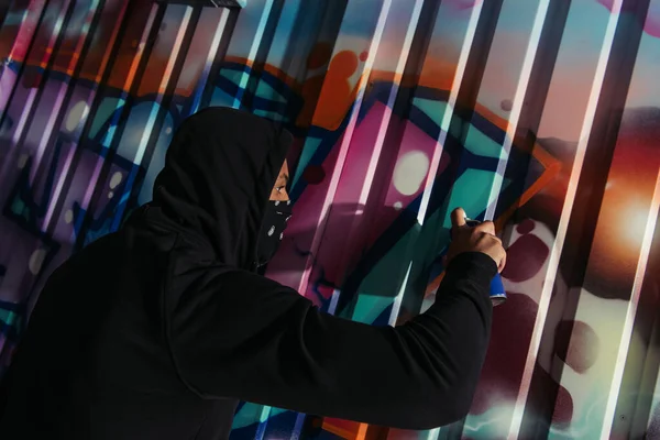 Вид збоку афроамериканського вандалу, що малює графіті на стіні на відкритому повітрі вночі — стокове фото
