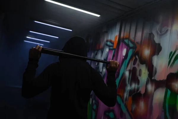Back view of african american hooligan holding baseball bat in garage with smoke and graffiti - foto de stock