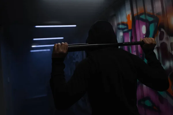 Back view of african american vandal in hoodie holding baseball bat in garage with graffiti - foto de stock