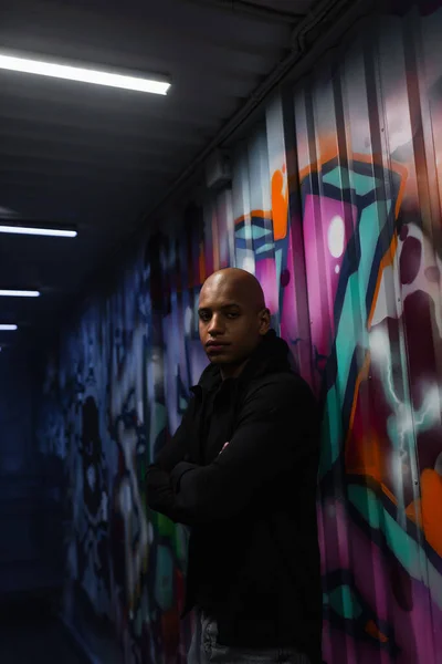 African american hooligan crossing arms near graffiti on wall in garage — Stock Photo