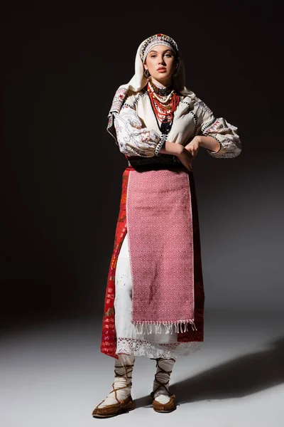 Full length of ukrainian woman in dress with ornament and red beads standing on black — Stock Photo