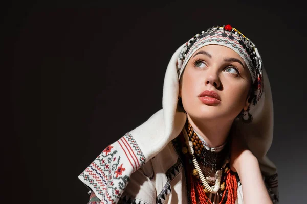 Portrait de jeune femme ukrainienne en vêtements traditionnels avec ornement et perles rouges regardant vers le haut sur noir — Photo de stock