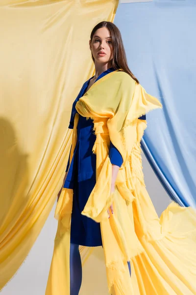 Young ukrainian woman in color block dress posing near blue and yellow curtains — Stock Photo