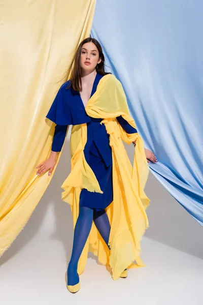 Volle Länge der stilvollen ukrainischen Frau in Farbe Block Kleid posiert in der Nähe von blauen und gelben Vorhängen — Stockfoto