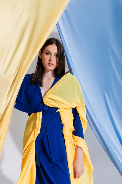 Ukrainerin in Farbblockkleid posiert in der Nähe blauer und gelber Vorhänge — Stockfoto