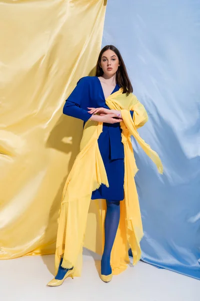 Full length of young ukrainian woman in color block clothes posing near blue and yellow curtains — Stockfoto