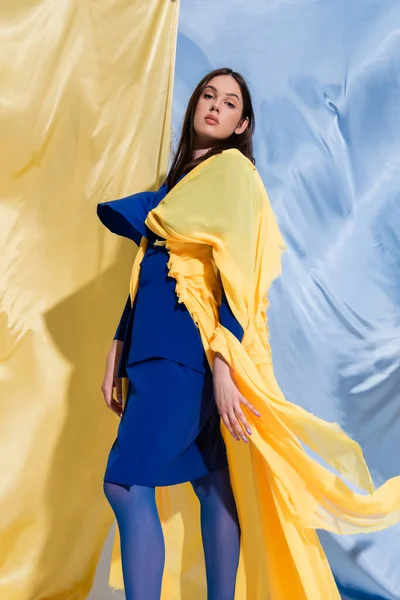 Confident young ukrainian woman in color block clothing posing near blue and yellow curtains — Foto stock