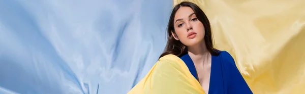 Young ukrainian woman in color block clothing posing near blue and yellow flag, banner — Fotografia de Stock