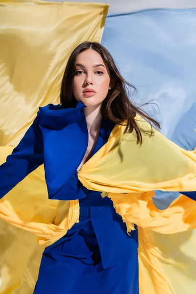 Stylish young ukrainian woman in color block clothing posing near blue and yellow flag — Foto stock