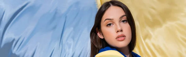 Patriotic young ukrainian woman looking at camera near blue and yellow flag, banner — Fotografia de Stock