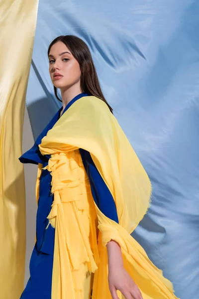 Mujer ucraniana joven en color bloque de ropa de pie cerca de tela azul y amarillo - foto de stock