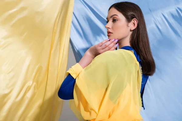 Jeune femme ukrainienne en couleur bloc vêtements regardant loin près de tissu bleu et jaune — Photo de stock