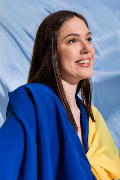 Pleased ukrainian woman in color block clothing posing near blue fabric — Fotografia de Stock