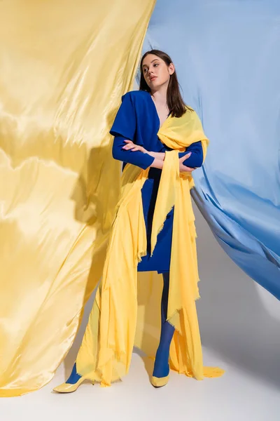 Full length of confident ukrainian woman in fashionable color block clothing posing near blue and yellow fabric — Stockfoto